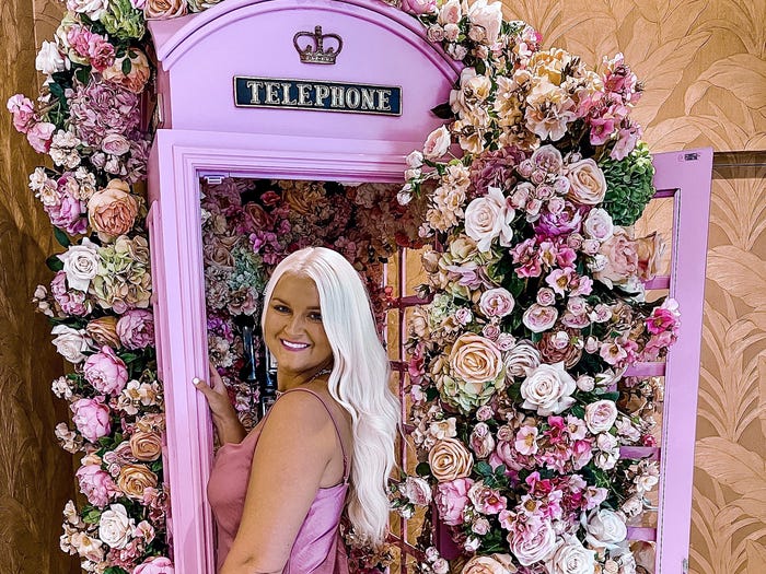 Katie in front of a hot pink telephone booth with roses exploding out from it