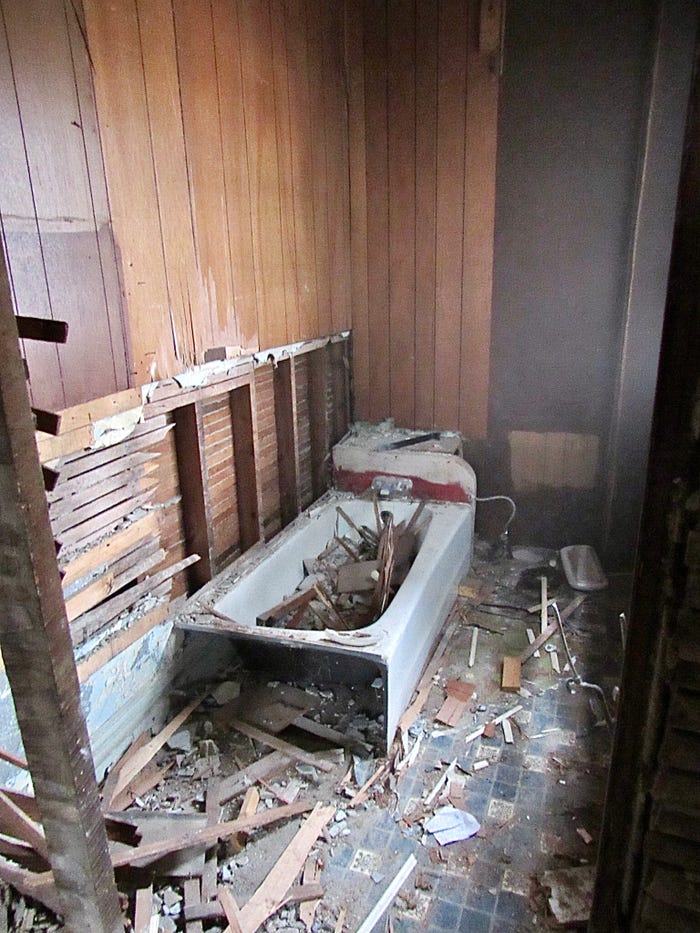 A destroyed bathroom with wood paneling falling off the walls