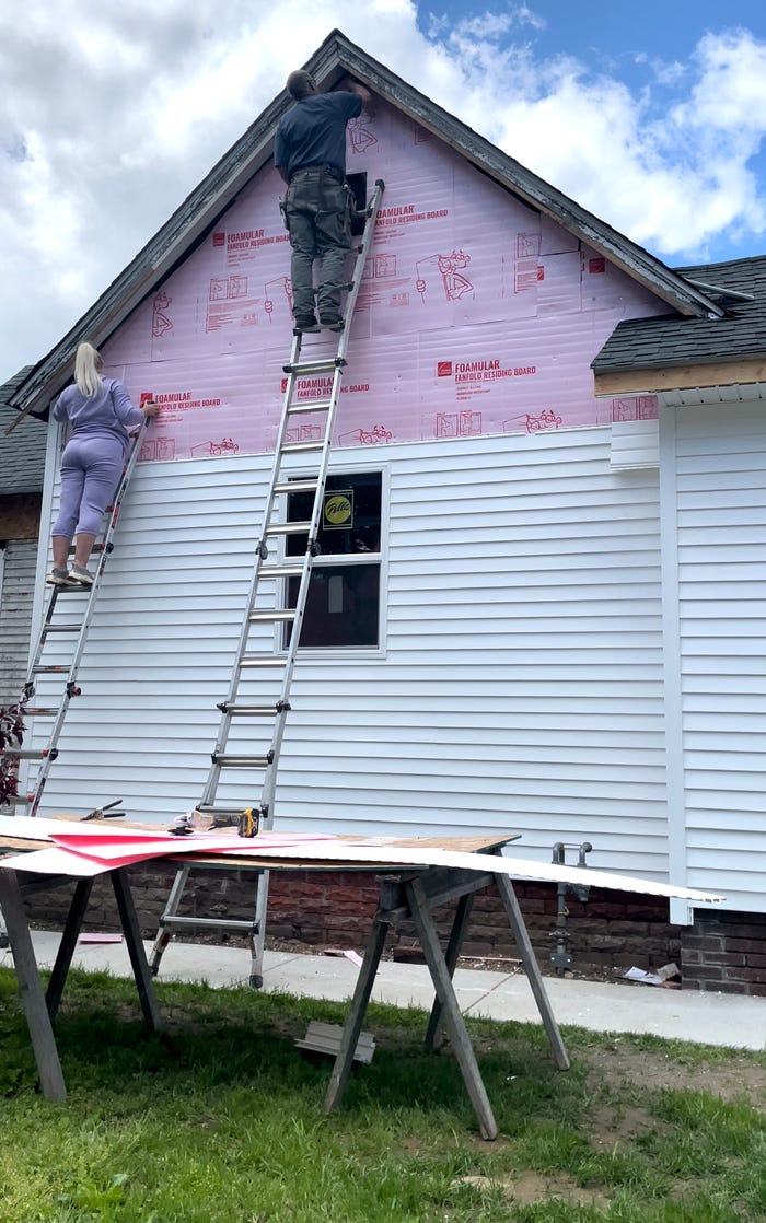 Katie and her father installing siding at the very top of the house.